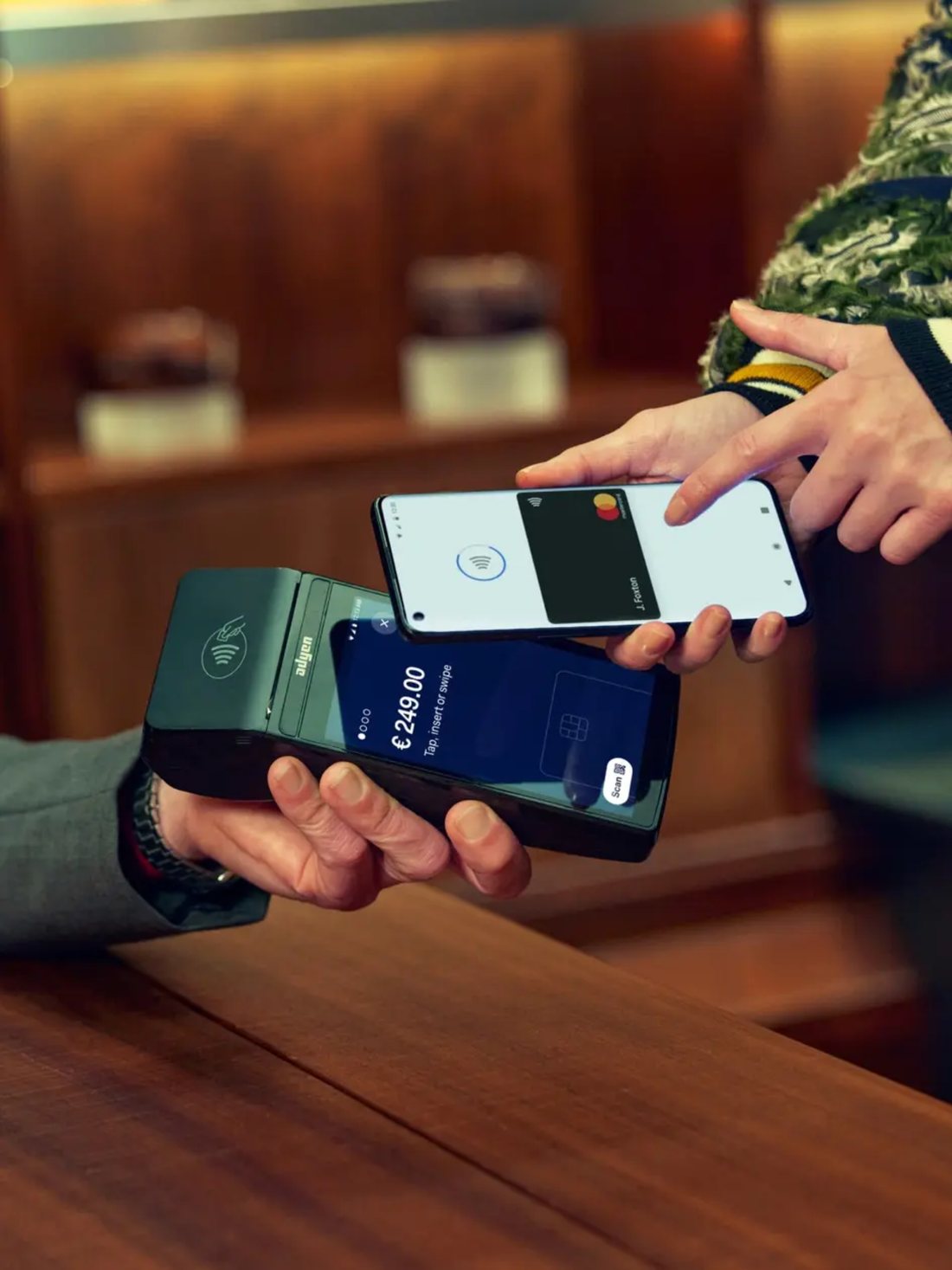 A guest tapping a phone wallet against a handheld terminal held by staff at a counter